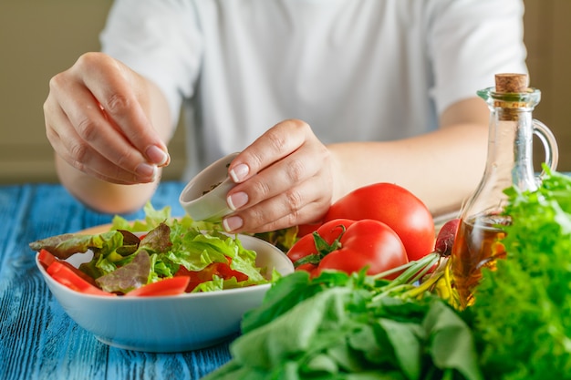 Mains de femme ajoutant des épices pour une salade de légumes