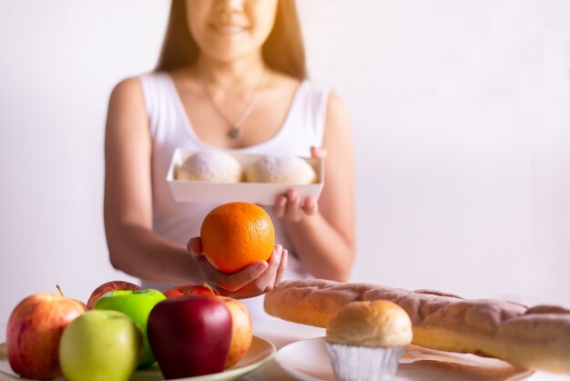 Mains de femme asiatique tenant orange et pain sur fond blanc, alimentation saine, concept de régime