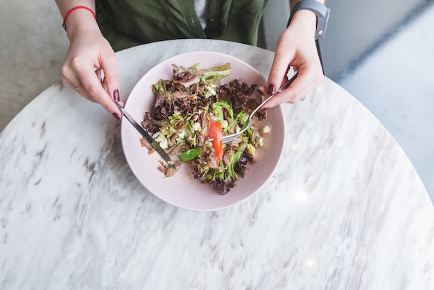 Mains de femme et assiette de salade. fille mangeant de la salade dans un restaurant léger à table donne sur le dessus.