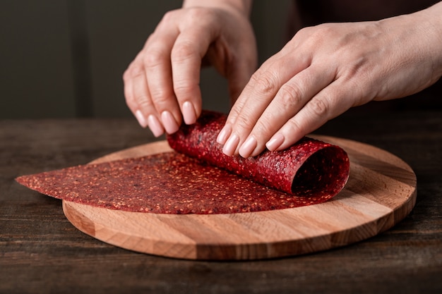 Mains de femme au foyer créative roulant du cuir de fruits fait maison sur planche de bois par table de cuisine tout en faisant des aliments savoureux et sains