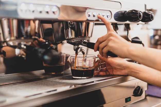 Mains de femme barista appuyant sur le bouton de la machine pour préparer du café frais.