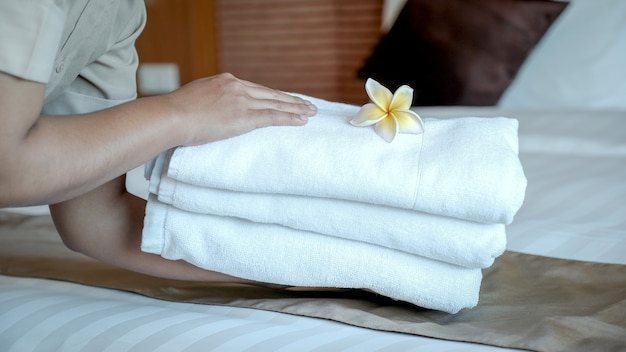 Mains de femme de chambre de l'hôtel mettant la fleur de frangipanier et les serviettes sur le lit dans la chambre d'hôtel de luxe prêt pour les voyages touristiques.