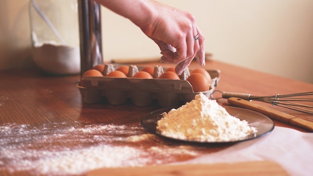 Les mains d'une femme chef cueillant un œuf pour faire de la pâte tout en faisant du pain avec un tas de blé à proximité