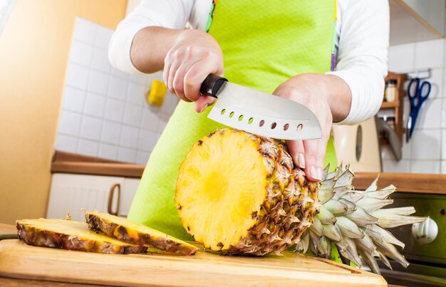 Les mains de la femme coupant l'ananas frais sur la cuisine