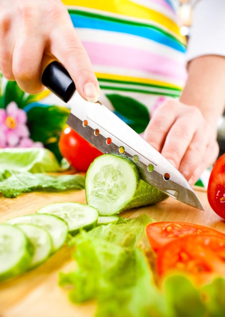 Mains de femme coupant le concombre, derrière les légumes frais.