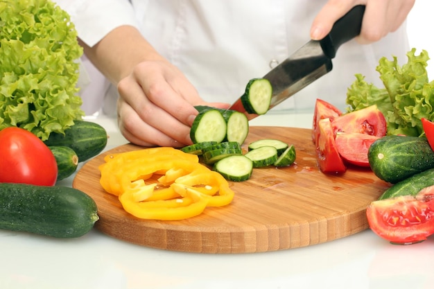 Mains de femme coupant des légumes sur le tableau noir de la cuisine