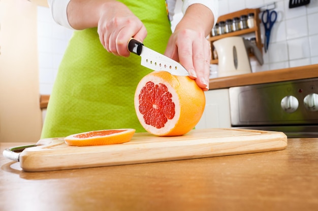 Les mains de la femme coupant le pamplemousse frais sur la cuisine