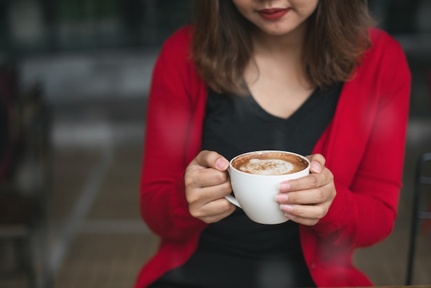 Les mains de la femme dans un cadigan rouge tenant une tasse de café cappucino en hiver.