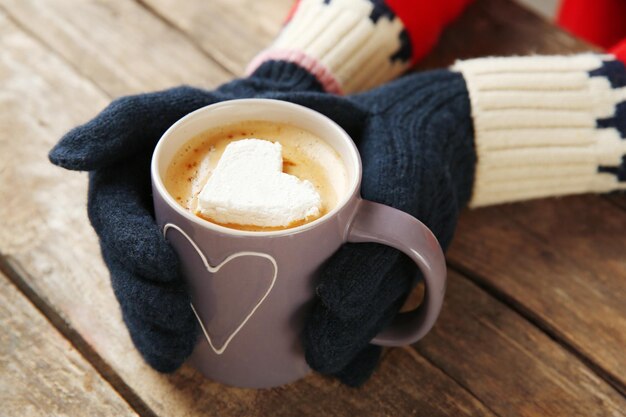 Mains de femme dans des mitaines tenant une tasse de café