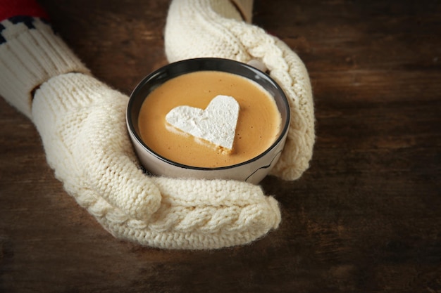 Mains de femme dans des mitaines tenant une tasse de café