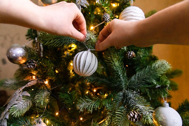 Mains de femme décorant l'arbre de Noël. Arbre de Noël avec décorations blanches et argentées, jouet d'ornements et boule. Design d'intérieur de style classique moderne. La veille de Noël à la maison, l'heure de la fête.