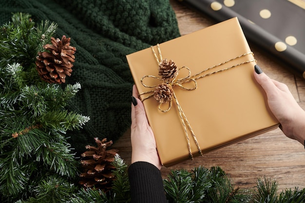 Mains de femme décorant des cadeaux de nouvel an avec du papier doré et des pommes de pin