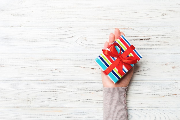 Des mains de femme donnent des cadeaux emballés de Noël ou autres vacances à la main dans du papier de couleur. Boîte à cadeaux, décoration de cadeau sur une table en bois rustique blanche, vue de dessus avec espace de copie