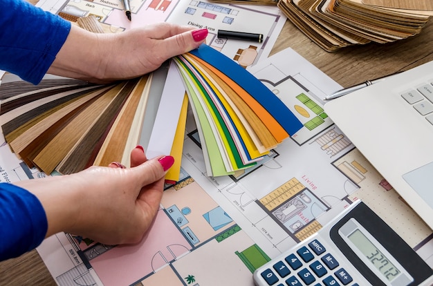 Mains de femme avec des échantillons de couleur, plan de maison, ordinateur portable et calculatrice