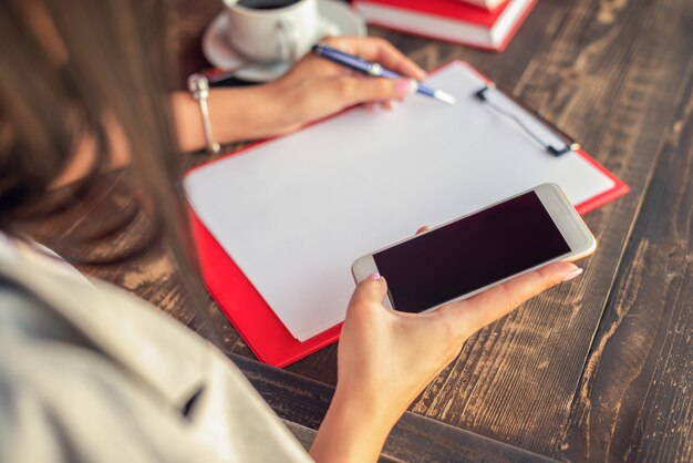 Les mains d'une femme écrivent sur un ordinateur portable et utilisent un smartphone sur une table en bois au café.