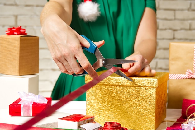 Photo mains de femme emballant un cadeau de noël dans une boîte en or avec un ruban rouge. emballage cadeau bricolage