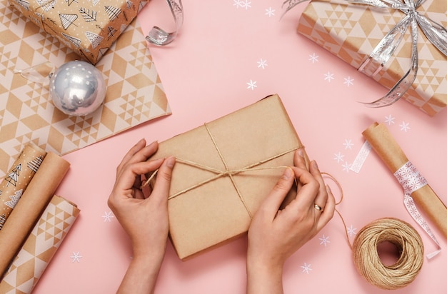 Mains de femme emballant des cadeaux dans du papier kraft. Vue de dessus.