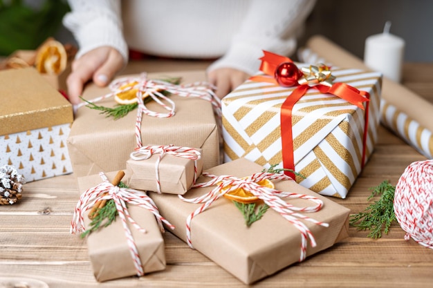 Les mains de la femme enveloppant le cadeau de noël bouchent les cadeaux non préparés sur fond de bois avec décor