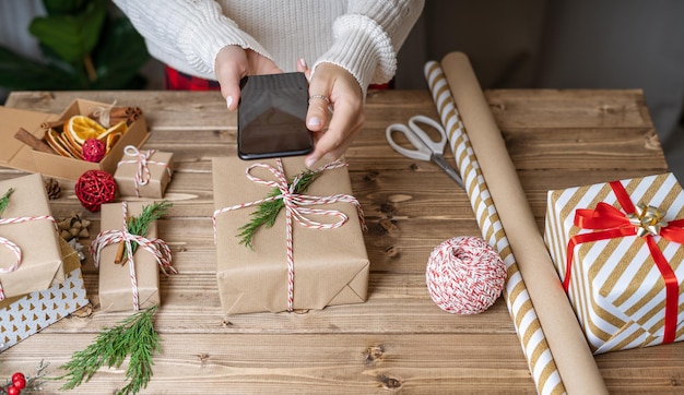 Les mains de la femme enveloppant le cadeau de Noël se bouchent et prennent des photos au téléphone des cadeaux non préparés