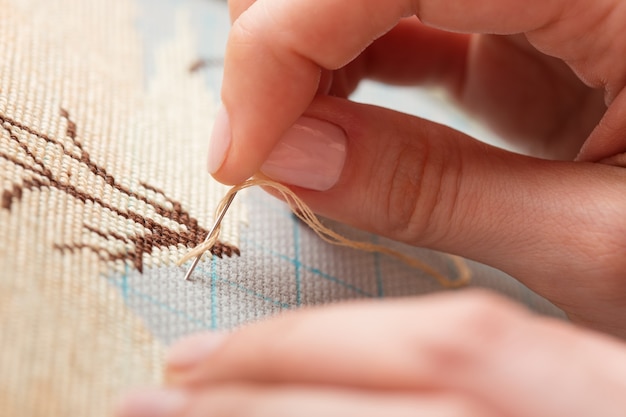 Mains de femme faisant du point de croix. Un gros plan de broderie.