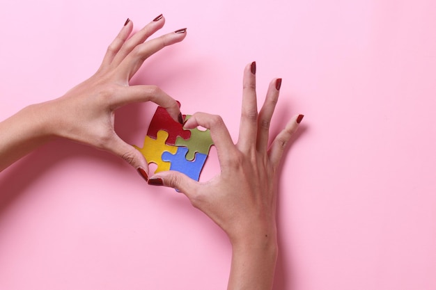 Mains de femme formant la forme de coeur sur un puzzle coloré isolé sur la couleur rose Journée mondiale de l'autisme