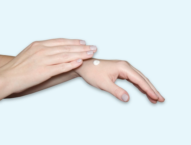 Les mains d'une femme, une goutte de crème hydratante blanche sur son bras. Soins des mains, hydratation de la peau