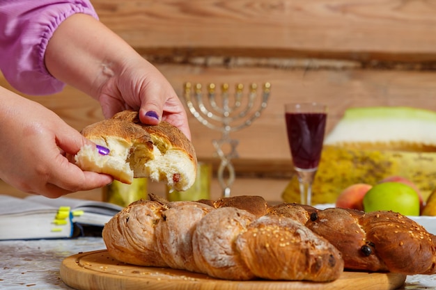 Les mains d'une femme juive cassent la challah pendant le repas de Shabbat avec une bénédiction