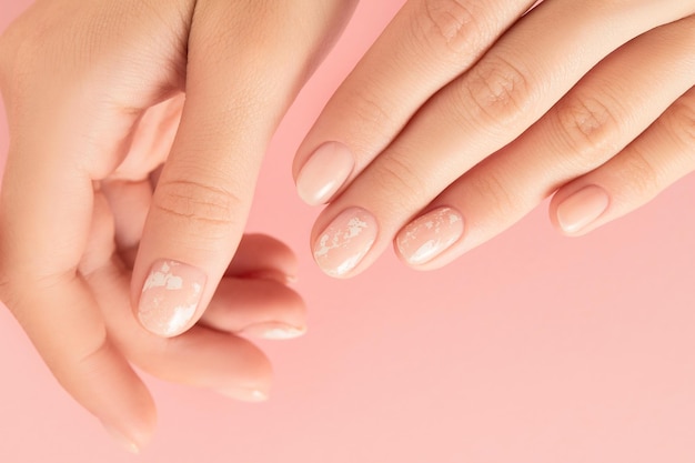 Mains de femme avec manucure nude à la mode sur fond rose design d'ongles d'été