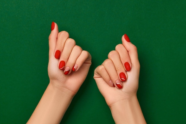 Mains de femme avec manucure rouge de Noël à la mode sur fond vert