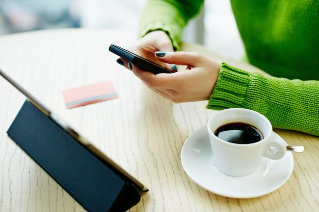 Mains de femme avec manucure sombre tenant le téléphone mobile, carte de crédit, tablette et tasse de café sur la table, concept indépendant, achats en ligne, mise à plat.