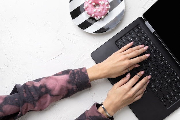 Les mains de la femme manucurée dans un sweat à capuche rose tendance tapant sur un ordinateur portable.