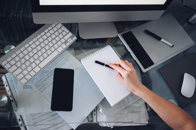 Mains de femme méconnaissables écrivant dans un cahier vide et un ordinateur. Pigiste utilisant un téléphone intelligent et un ordinateur portable à la maison pendant la quarantaine. Marketing Internet, finance, entreprise, concept de travail à distance