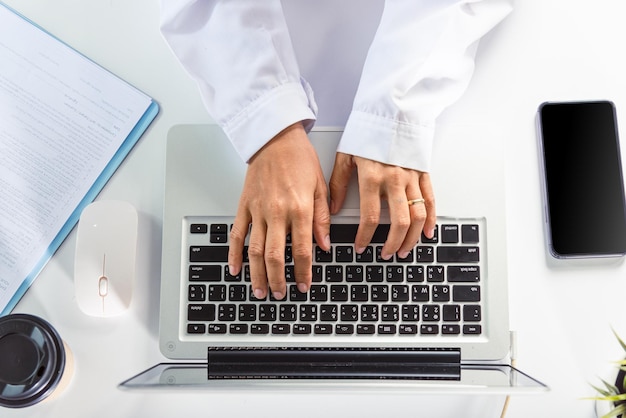 Les mains d'une femme médecin portent un uniforme à l'hôpital, elle tape des informations sur un ordinateur portable à clavier