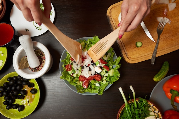 Mains de femme mélangeant une salade grecque saine