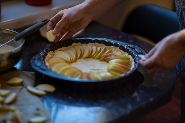 mains de femme mettent des pommes sur la pâte dans la cuisine