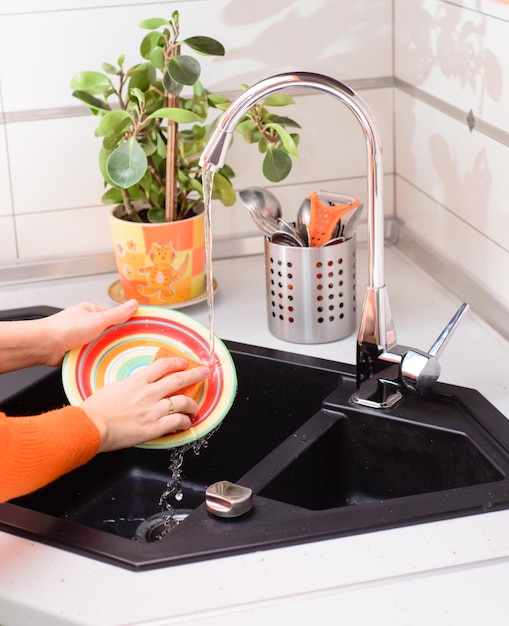 mains de femme nettoie la vaisselle dans la cuisine