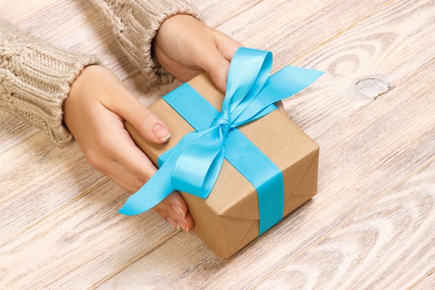 Les mains de la femme offrent un cadeau fait main de vacances de Saint Valentin emballé dans du papier kraft avec un ruban bleu