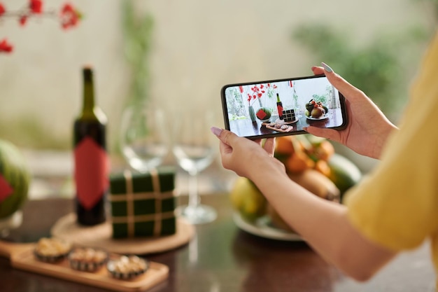 Mains de femme photographiant la table du dîner servie pour la célébration du tet