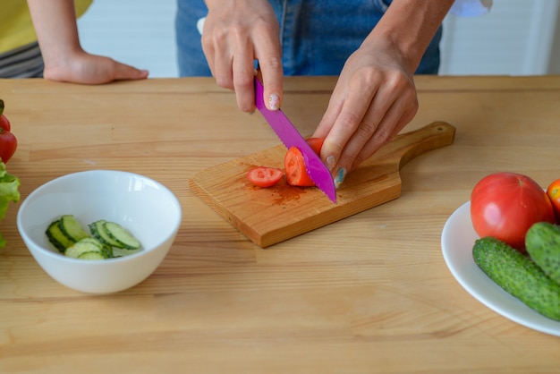 Mains de femme de plan rapproché coupant des légumes de concombre par couteau