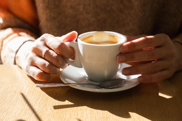 Mains d'une femme prenant un café avec la lumière du matin