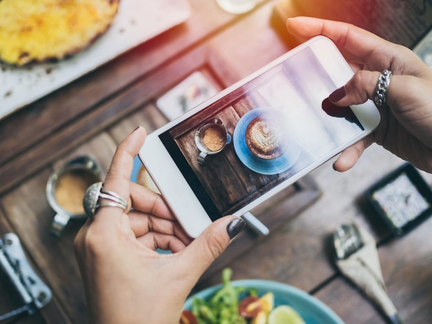 Mains de femme prenant la photo d'une tasse de café sur une table en bois par smartphone