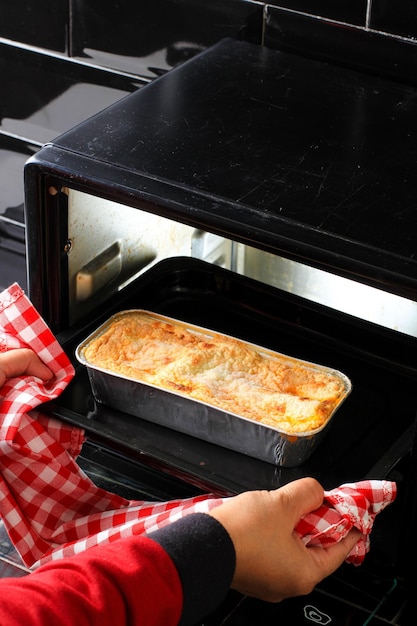 Mains de femme prenant la plaque de cuisson avec des lasagnes hors du four