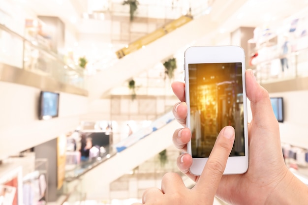 Mains de femme Prendre une photo avec un téléphone intelligent dans un centre commercial avec une image floue d'un magasin de vêtements.