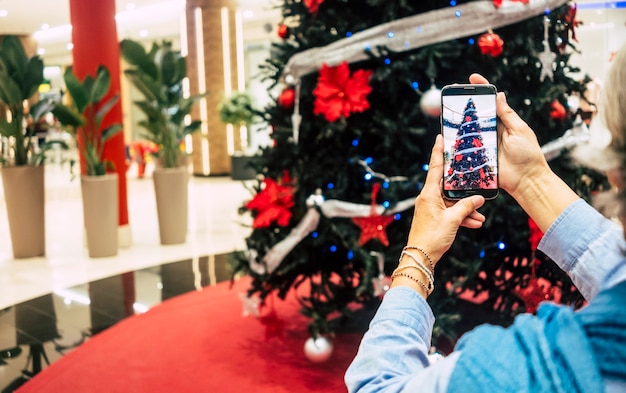 Les mains de la femme prennent une photo du bel arbre de Noël dans le centre commercial - concept de vacances et de consommation