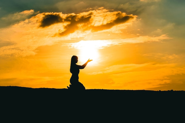 Mains de femme priant pour la bénédiction de Dieu sur fond de coucher de soleil