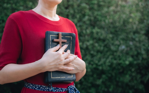 Les mains de la femme prient avec la bible et la croix en bois