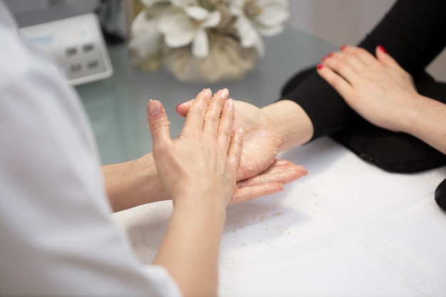 Mains de femme recevant un gommage des mains peeling par une esthéticienne dans un salon de beauté. Manucure SPA, massage des mains et soins du corps