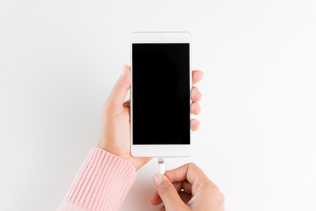 Mains de femme reliant le chargeur à un smartphone sur fond de tableau blanc