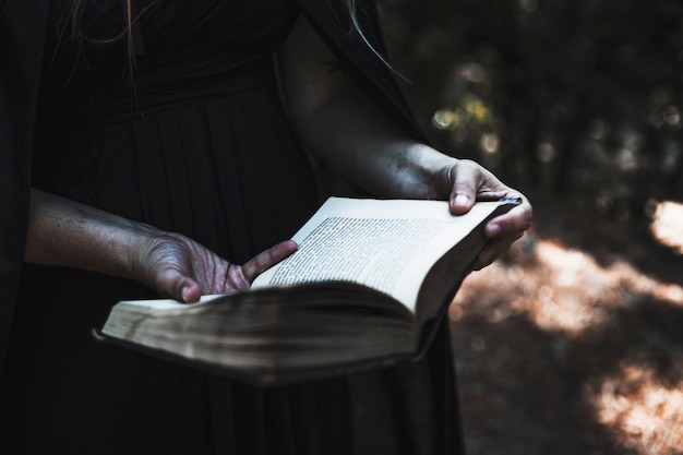 Mains de femme en robe noire et manteau tenant livre ouvert