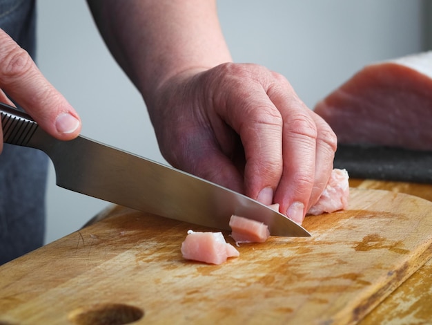 Mains d'une femme seigners coupant un filet de viande de porc cru sur une planche de bois avec un couteau